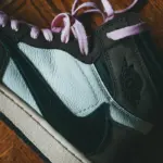 Modern black sneaker with pink laces placed on wooden floor