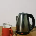 Stainless steel electric kettle with red coffee mug on wooden table