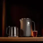 Black electric kettle with glass jug and filled cup on wooden table