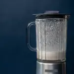 Close-up silver blender making milkshake on blue background studio shot