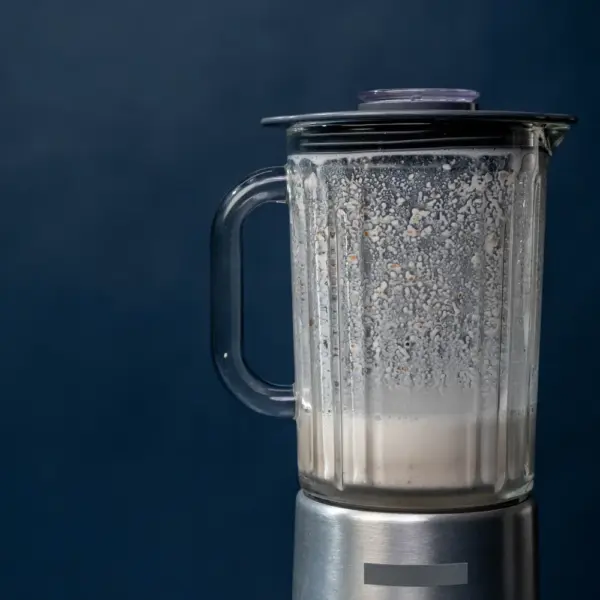 Close-up silver blender making milkshake on blue background studio shot